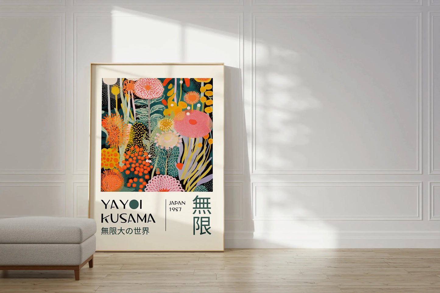 A framed art print featuring a colorful abstract floral design with Japanese text, leaning against a white paneled wall on a light wood floor next to a gray bench.