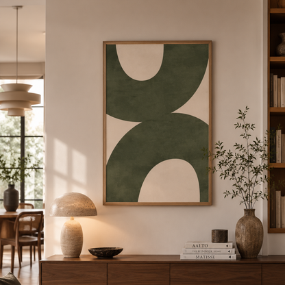 A framed abstract art print featuring large organic shapes in dark green and cream, displayed on a beige wall above a wooden console table in a modern, sunlit living room.