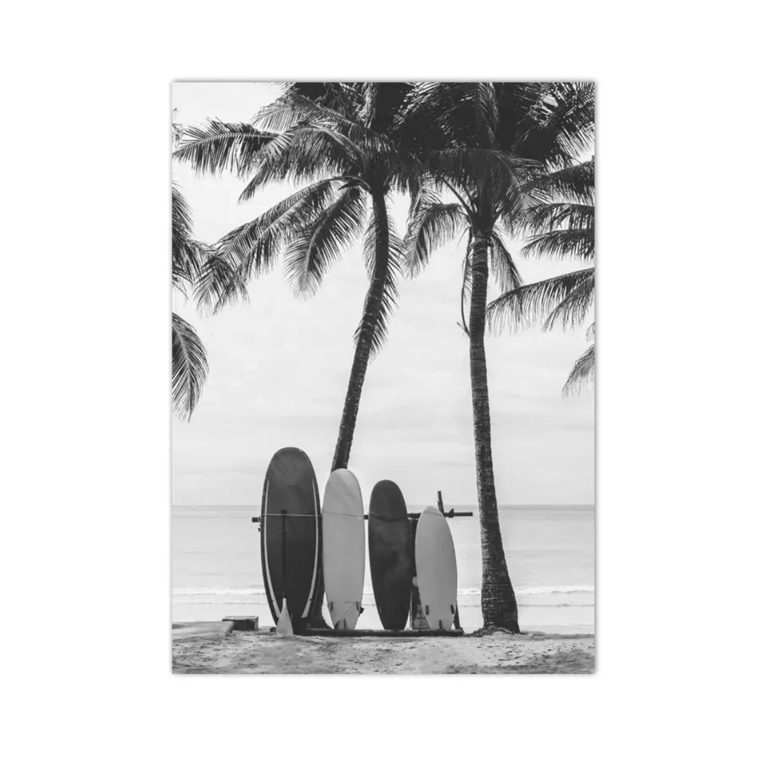 Black and white photographic print of four surfboards leaning against palm trees on a sandy beach with the ocean in the background.