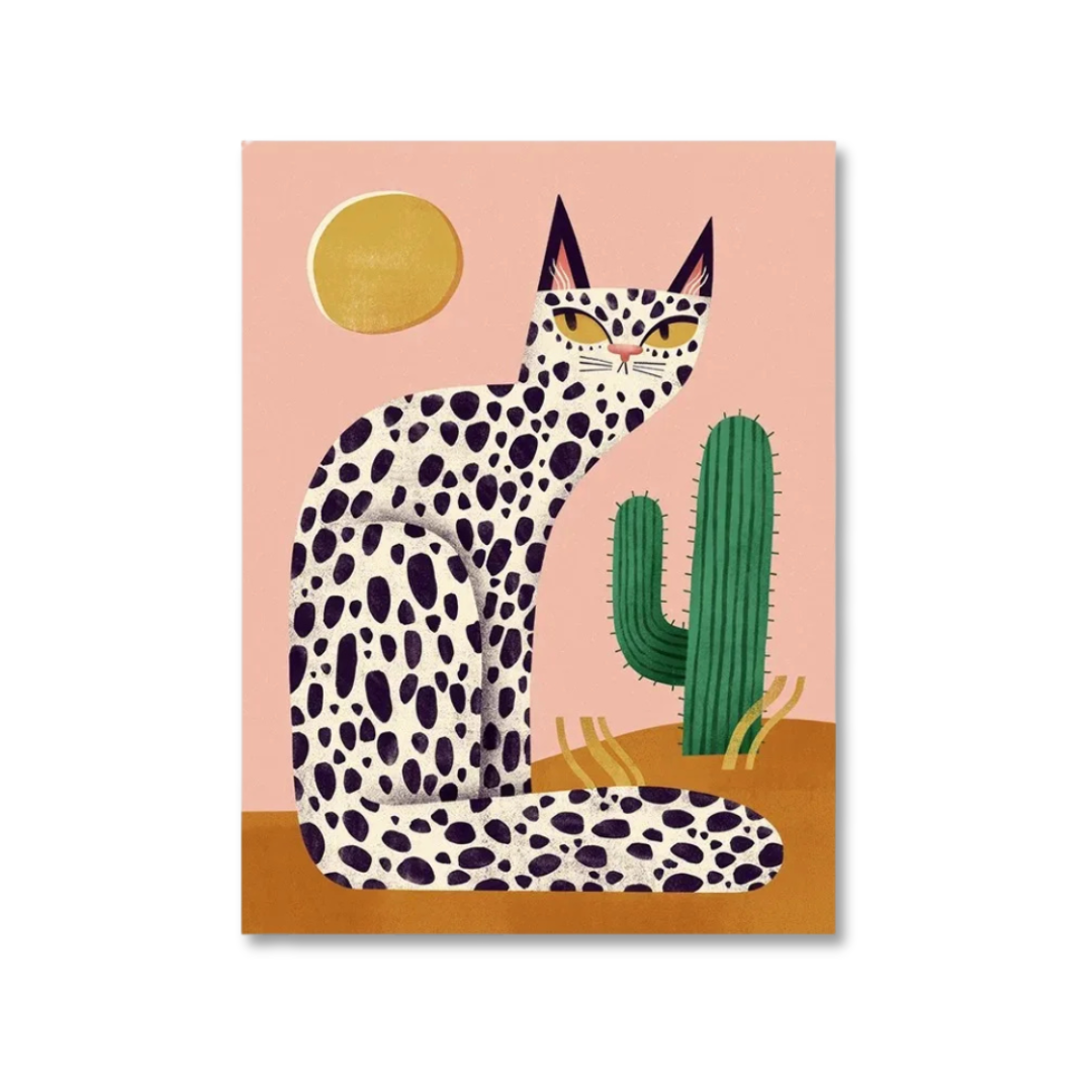 A stylized art print featuring a spotted cat in a desert scene with a cactus, sun, and pink sky, shown as a rectangular print on a white background.