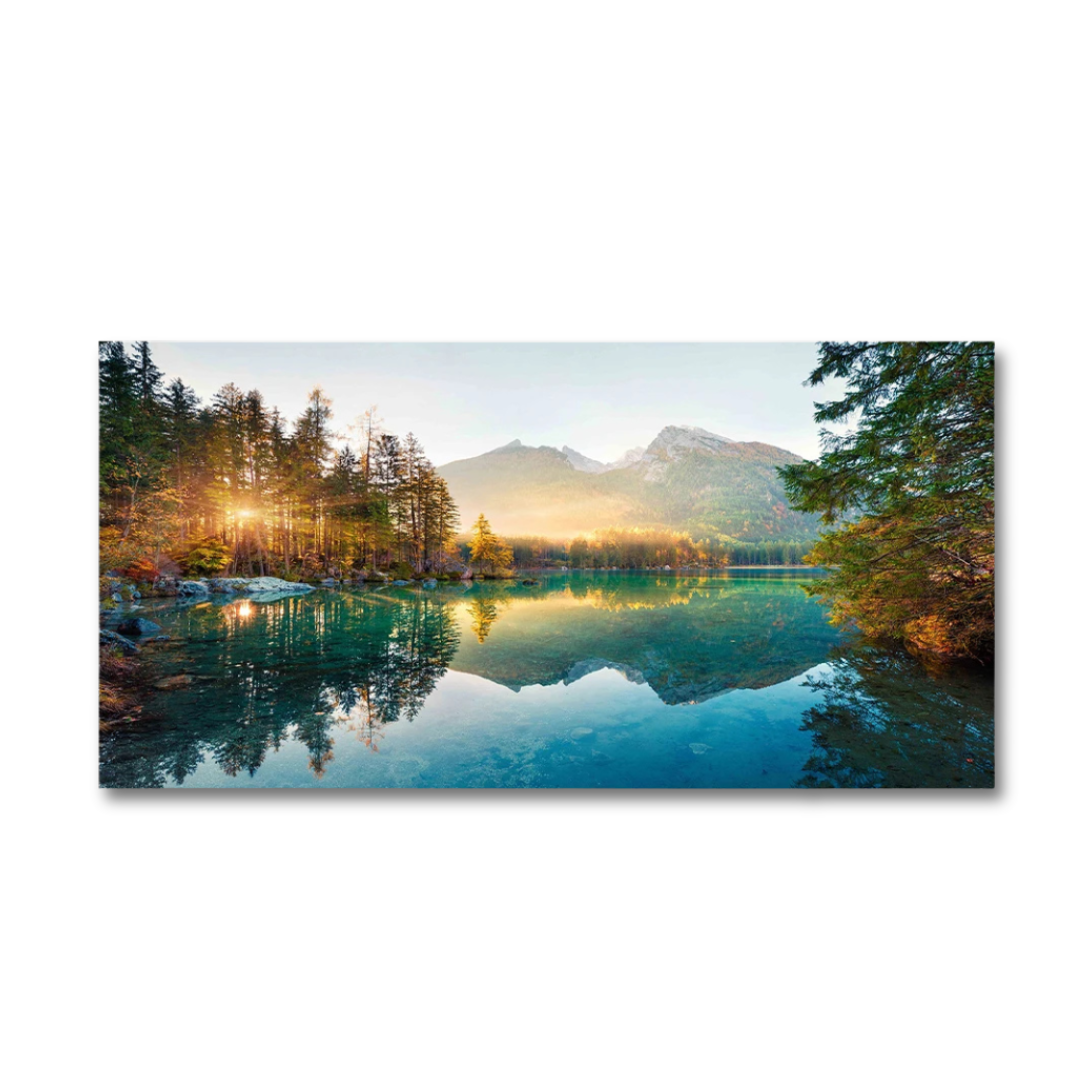 A panoramic landscape canvas print depicting a serene mountain lake at sunrise, with golden sunlight filtering through pine trees and reflecting perfectly on the calm water, shown against a plain white background.