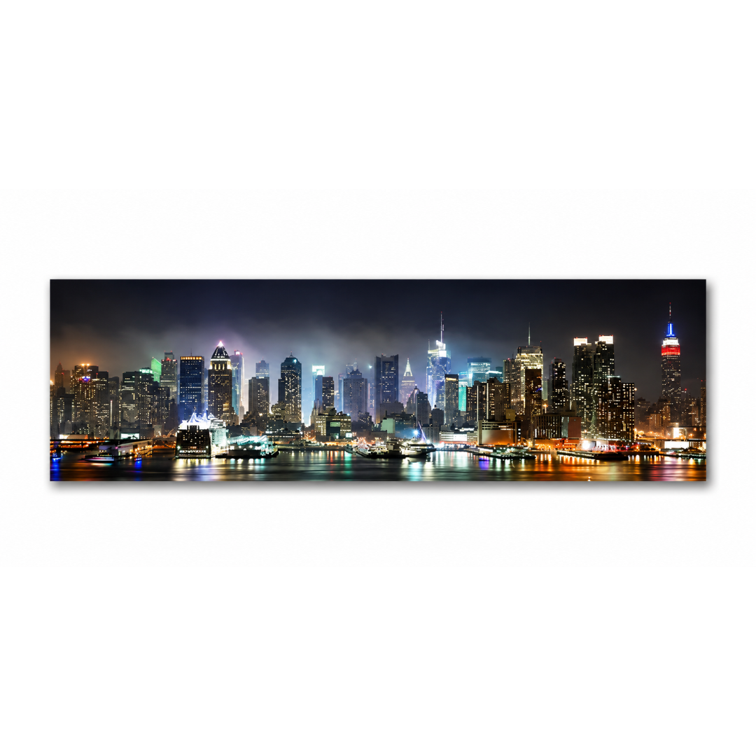 A panoramic canvas print of the New York City skyline at night, featuring illuminated skyscrapers and reflections on the water, displayed against a solid white background.