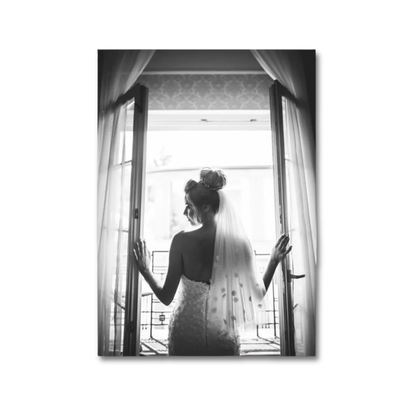 A black and white vertical photographic print of a bride in a wedding dress and veil standing in front of open double doors, shown against a plain white background.