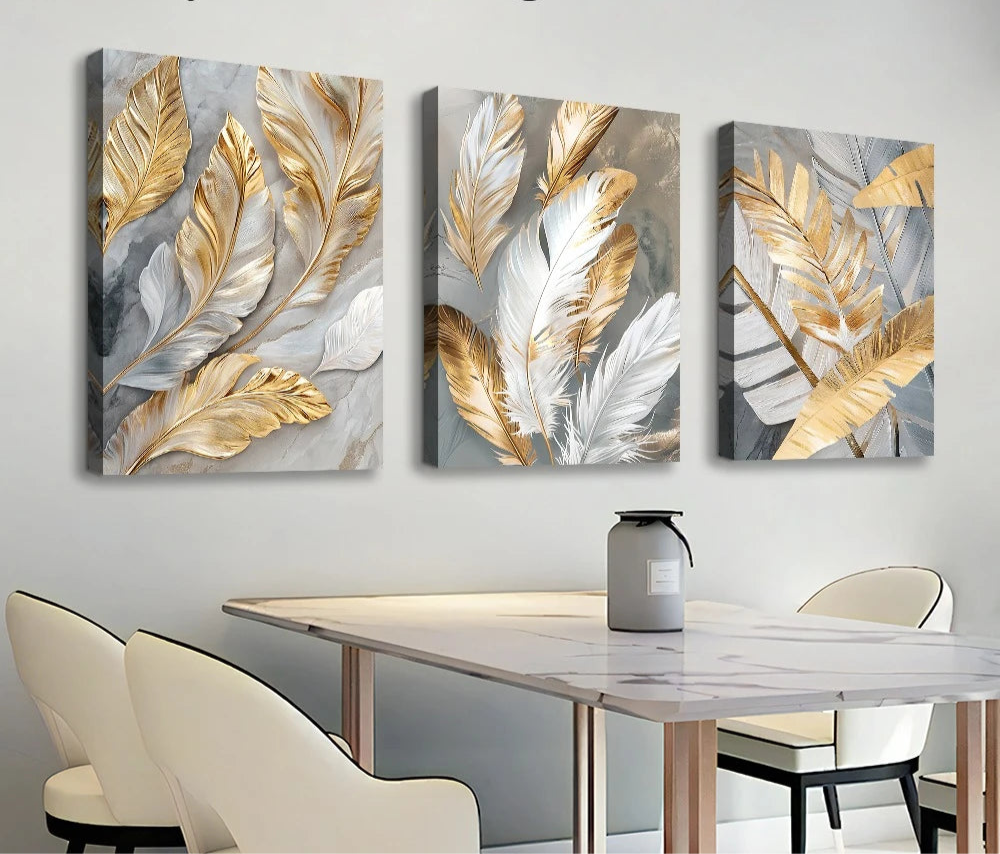 Three abstract wall art pieces with gold and silver leaves on a white wall above a dining table.