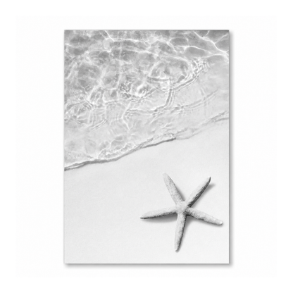 A vertical black and white photographic print of a beach scene, featuring a starfish on the sand beneath rippling ocean water, shown as a mockup against a white background.