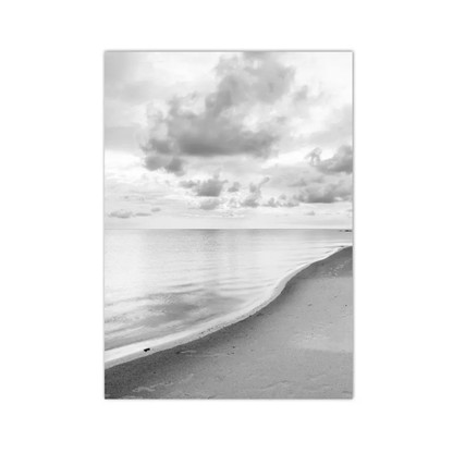 A black and white landscape photograph print of a beach shoreline under a cloudy sky, displayed as a vertical rectangular art piece against a white background.