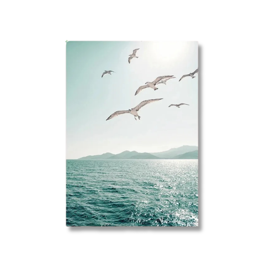 A vertical canvas wall art print depicting a scenic view of seagulls flying over a turquoise blue ocean with distant mountains under a bright sky, shown against a plain white background.