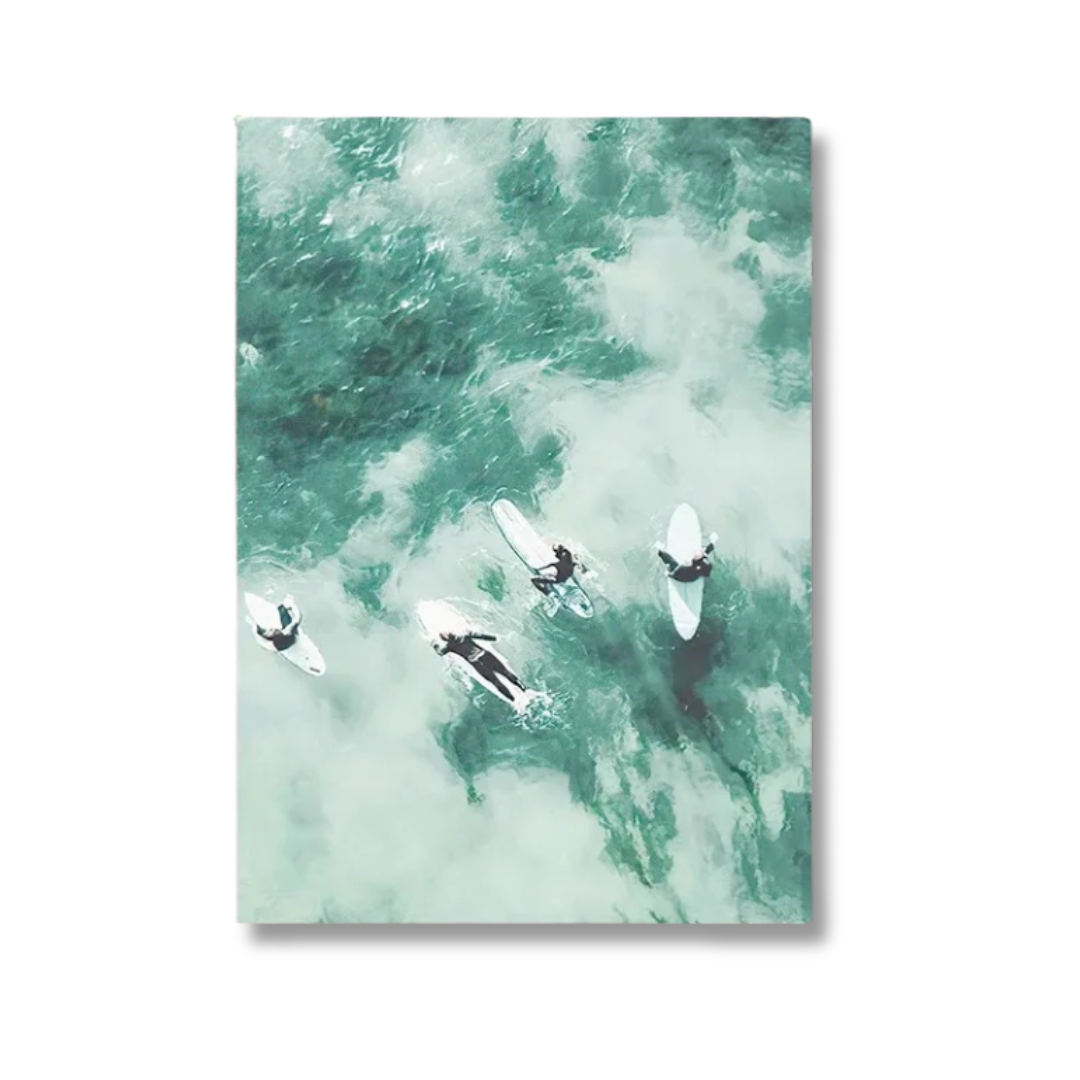 A vertical canvas wall art print featuring an aerial photograph of surfers riding through green and white ocean waves, shown against a plain white background.
