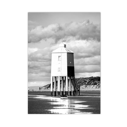 A black and white photographic print of a tall wooden tide lighthouse standing on stilts in shallow water under a dramatic cloudy sky.